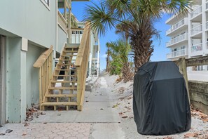 A narrow pathway with a wooden staircase leading to a building, a covered object, and a palm tree. - Paradise on the Sea (Englewood)
