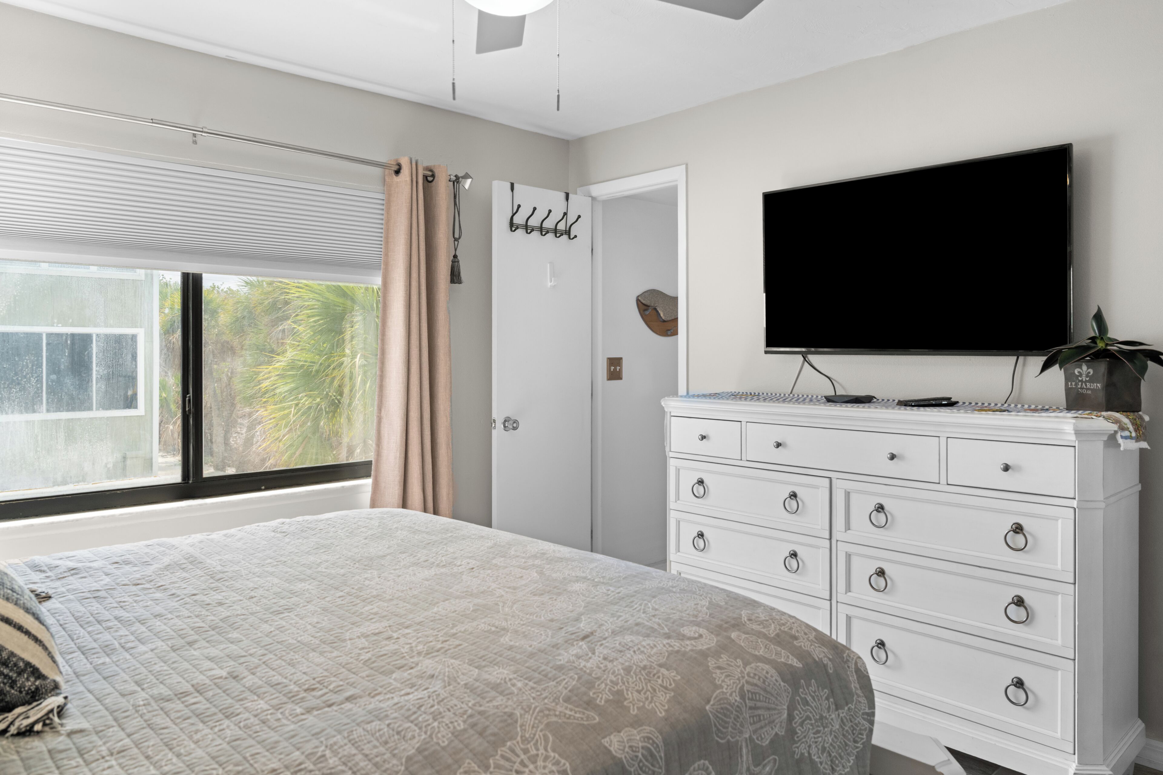 A bedroom with a bed, a dresser, a television, and a window with curtains.