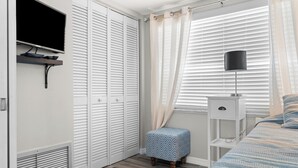 A bedroom with a bed, a bedside table, a lamp, a TV mounted on the wall, and a closet with sliding doors. - Paradise on the Sea (Englewood)