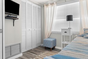 A bedroom with a bed, a bedside table, a lamp, a TV mounted on the wall, and a closet with sliding doors. - Paradise on the Sea (Englewood)
