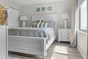 A bedroom with a bed, nightstands, a window, and a wall with framed artwork. - Paradise on the Sea (Englewood)