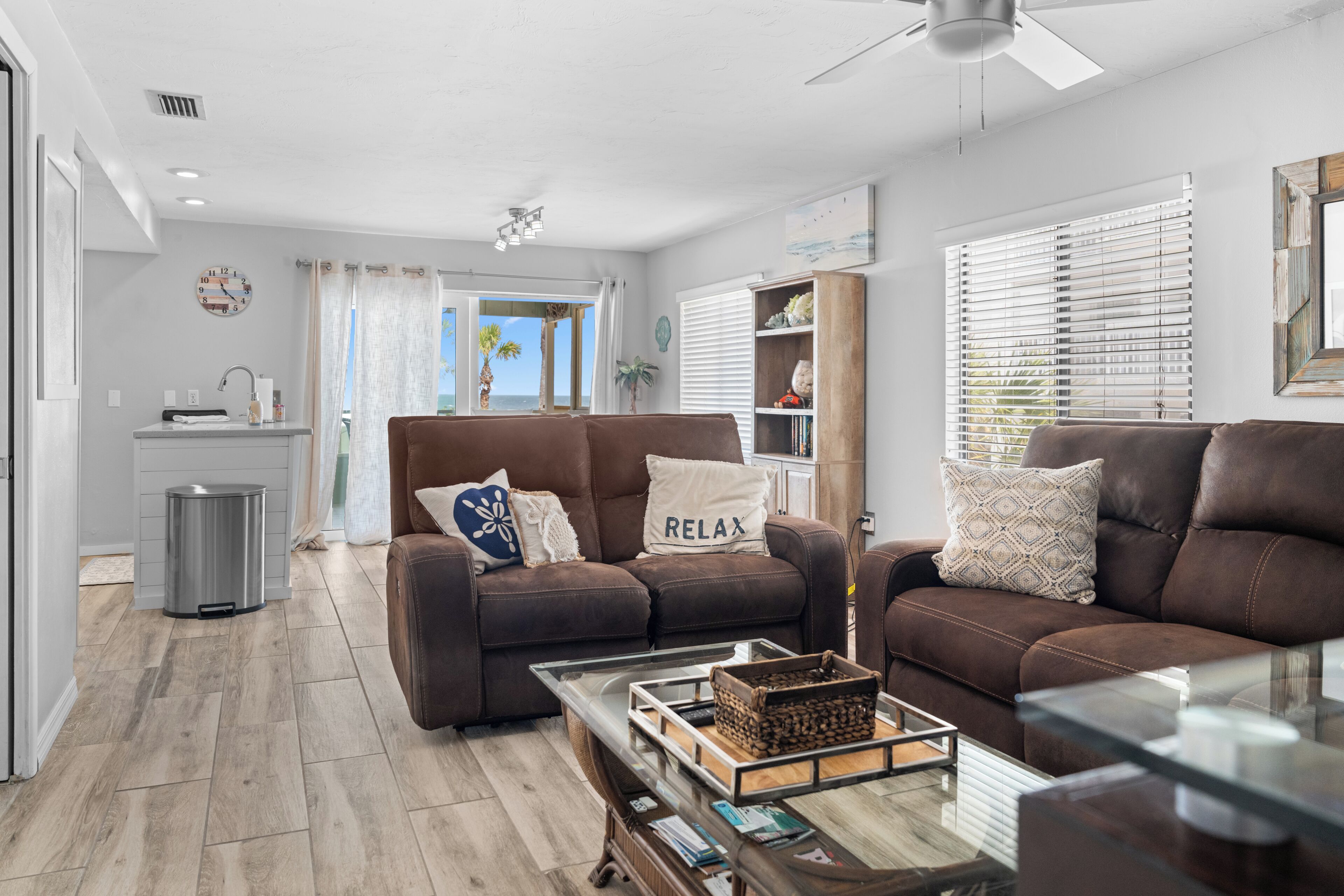 A modern living room with a brown leather sofa, a coffee table, and a view of the ocean through the window.