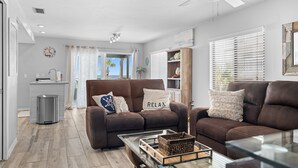 A modern living room with a brown leather sofa, a coffee table, and a view of the ocean through the window. - Paradise on the Sea (Englewood)