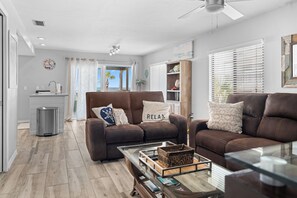 A modern living room with a brown leather sofa, a coffee table, and a view of the ocean through the window. - Paradise on the Sea (Englewood)