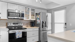 A modern kitchen with stainless steel appliances, white cabinetry, and a tiled backsplash. - Paradise on the Sea (Englewood)
