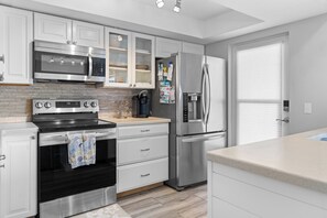 A modern kitchen with stainless steel appliances, white cabinetry, and a tiled backsplash. - Paradise on the Sea (Englewood)