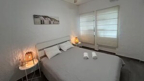 Et soveværelse med en seng, to sengeborde med lamper, en loftventilator og et vindue med skodder.