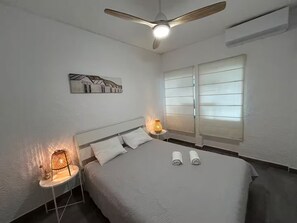 Ein Schlafzimmer mit einem Bett, zwei Nachttischlampen, einem Deckenventilator und einem Fenster mit Jalousien.