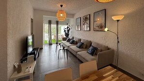 En moderne stue med sofa, sofabord og fjernsyn. Der er to hængende lamper og en gulvlampe.