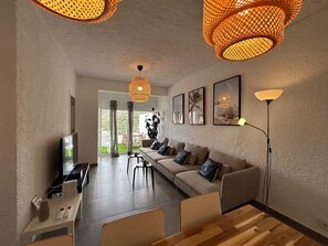 Ein modernes Wohnzimmer mit Sofa, Couchtisch und Fernseher. Zwei Pendelleuchten und eine Stehlampe sind vorhanden.