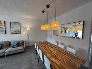A modern living room with a wooden dining table, a sofa, and a floor lamp. - Sail guest house (Sesimbra)