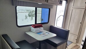 Ett litet, praktiskt kök med ett fönster, ett litet bord med handdukar och en bänk.