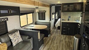 Interior compacto de una caravana con kitchenette, zona de estar y una pequeña mesa de comedor.