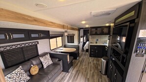 Interior compacto de una caravana con kitchenette, zona de comedor y sala de estar con sofá y cojines.