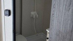 Un baño pequeño con inodoro, cabina de ducha y un mueble de almacenamiento.