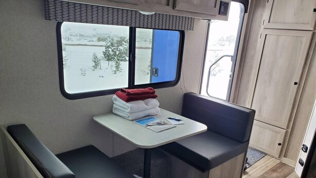 Una kitchenette compacta con ventana, una mesita con toallas y un banco.