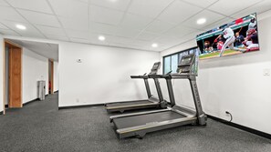 Ein Fitnessraum mit Laufbändern, einem Wasserspender und einem Fernseher an der Wand.
