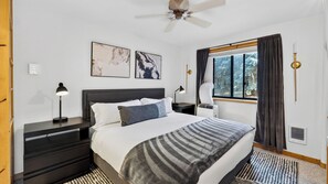 Ein Schlafzimmer mit einem Bett, Nachttischen, einem Deckenventilator, einem Fenster mit Vorhängen und Kunstwerken an der Wand.