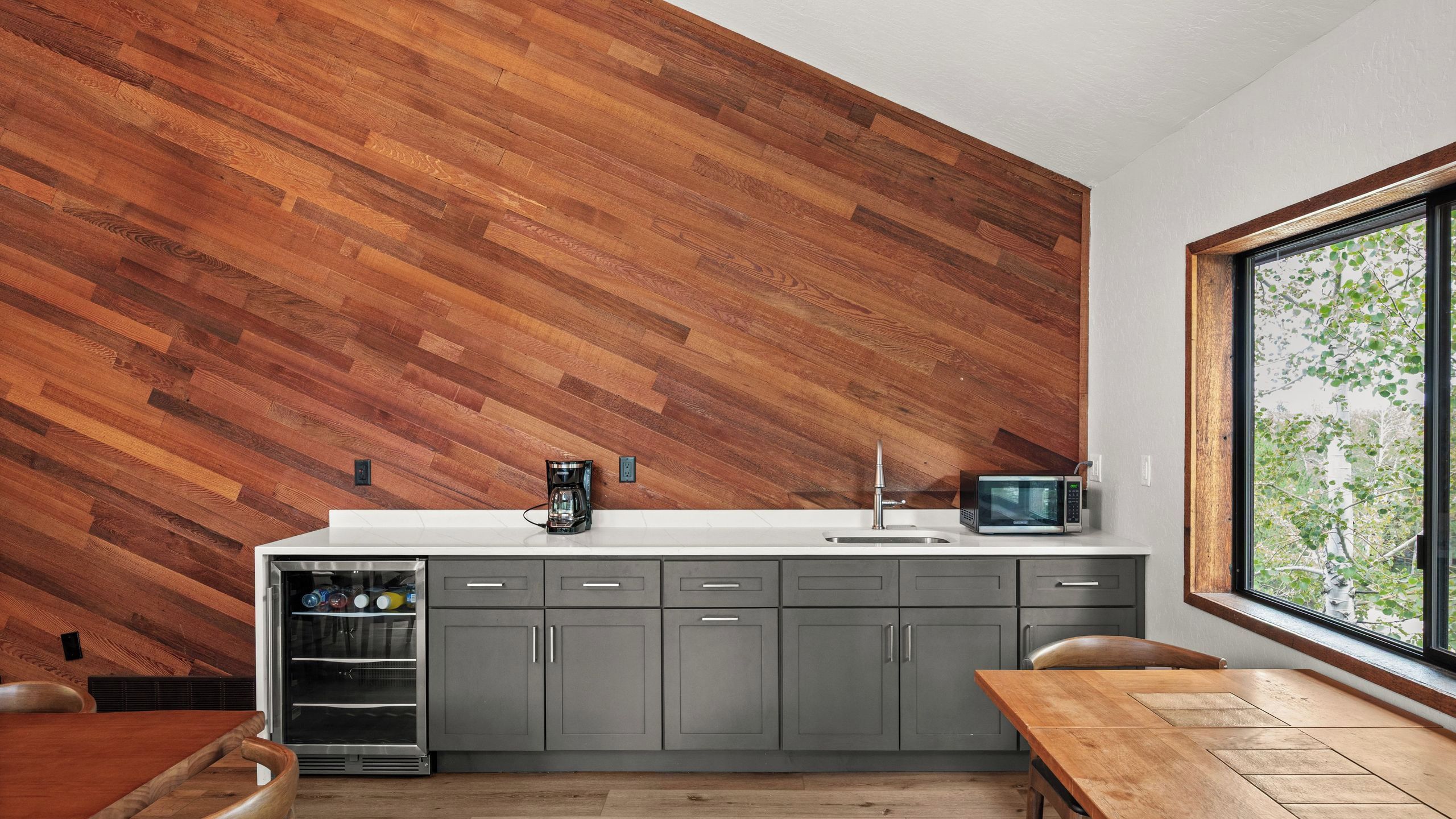 A modern kitchen with a wooden wall, grey cabinets, a stainless steel sink, and a microwave.