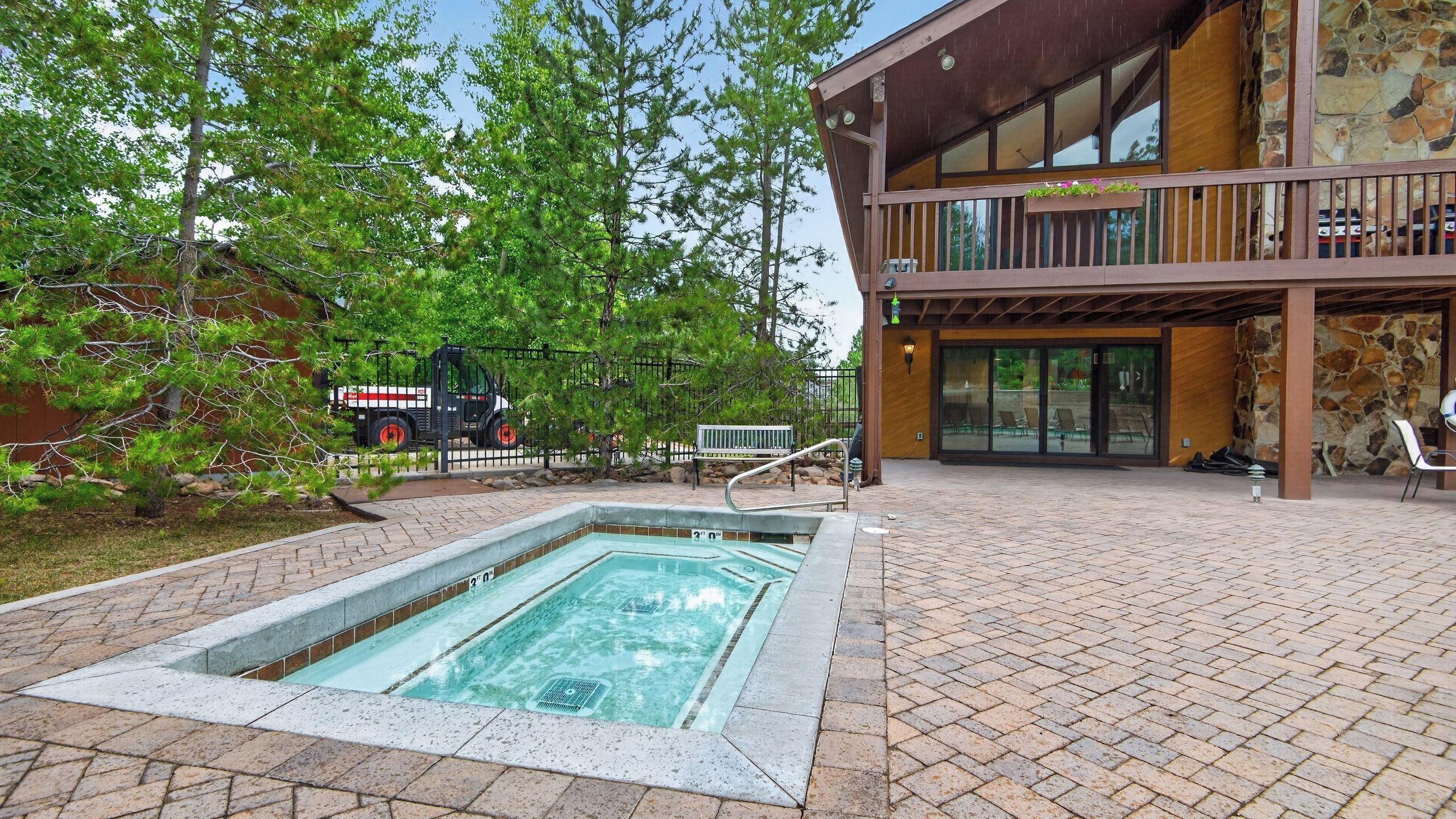 A swimming pool with a wooden deck, a covered outdoor seating area, and a building with stone walls.