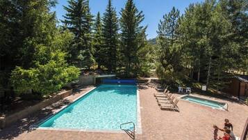 A rectangular swimming pool with a diving board, surrounded by trees and a brick patio.