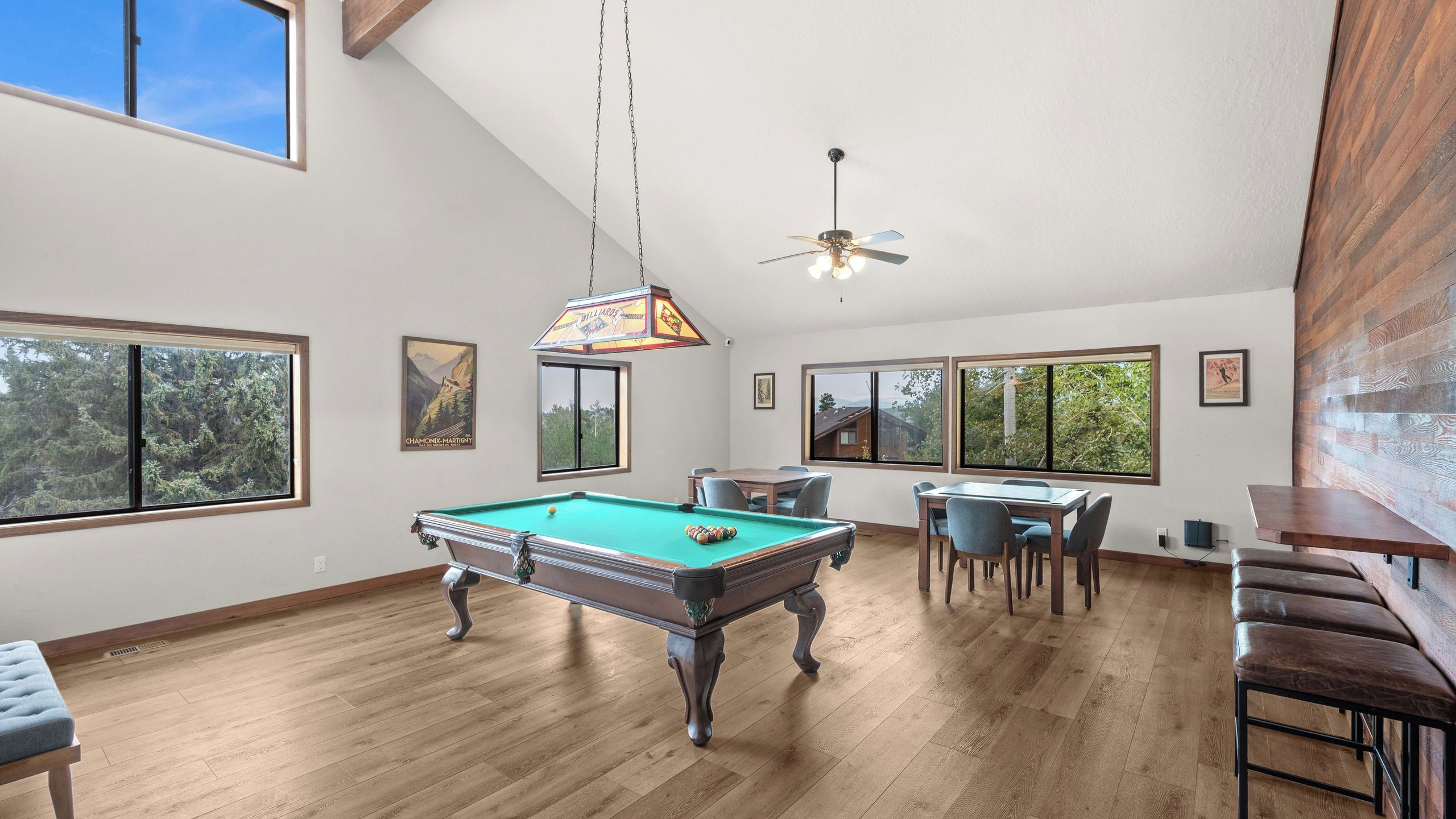 A spacious room with a pool table, dining area, and large windows offering views of the outdoors.
