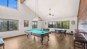 A spacious room with a pool table, dining area, and large windows offering views of the outdoors.