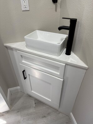 A bathroom with a white vanity, a black faucet, and a white basin.