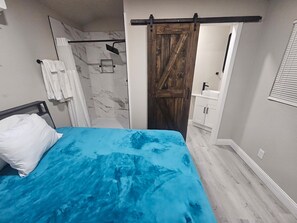 A bedroom with a bed, a shower, and a bathroom with a sink and cabinets.