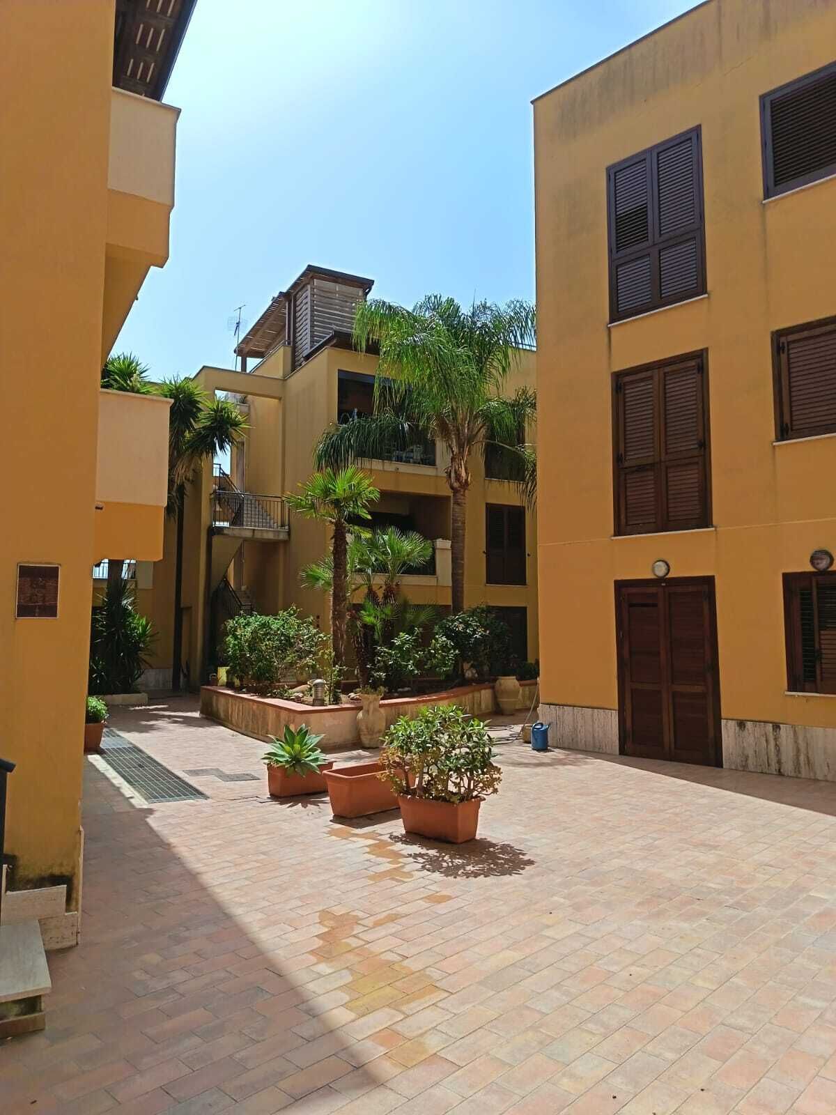 A courtyard with potted plants, a tiled floor, and buildings with balconies and windows.
