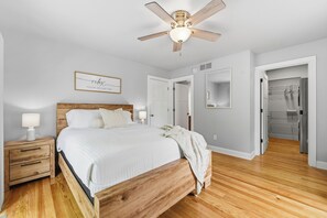 A bedroom with a wooden bed, a nightstand, a ceiling fan, and a wall-mounted mirror. - Stay at Bree's Retreat! Spacious 5BR Pet-Friendly- 5 Mins to Beach-Large Yard! (South Haven)