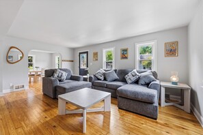 A modern living room with grey sofas, a white coffee table, and hardwood flooring. - Stay at Bree's Retreat! Spacious 5BR Pet-Friendly- 5 Mins to Beach-Large Yard! (South Haven)
