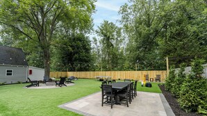 Un cortile con patio, mobili da esterno, barbecue e recinzione in legno.