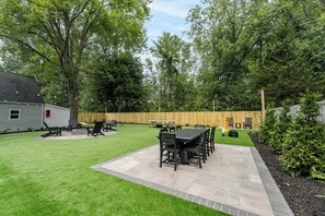 Ein Garten mit Terrasse, Gartenmöbeln, einem Grill und einem Holzzaun.