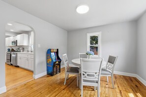 A modern kitchen with white cabinets, a dining area with a table and chairs, and a Pac-Man arcade game. - Stay at Bree's Retreat! Spacious 5BR Pet-Friendly- 5 Mins to Beach-Large Yard! (South Haven)