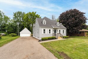 A single-story house with a front garage, a driveway, and a well-maintained lawn. - Stay at Bree's Retreat! Spacious 5BR Pet-Friendly- 5 Mins to Beach-Large Yard! (South Haven)