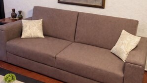 A living room with a brown sofa, two decorative pillows, a framed artwork on the wall, and a small table with a plant. - Private 2-bedroom apartment in the heart of Cancun (pet-friendly) (Cancún)