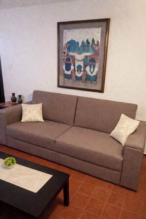 A living room with a brown sofa, two decorative pillows, a framed artwork on the wall, and a small table with a plant. - Private 2-bedroom apartment in the heart of Cancun (pet-friendly) (Cancún)