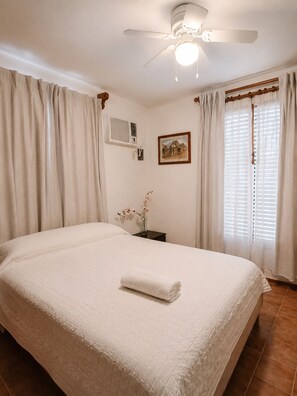A bedroom with a bed, a ceiling fan, an air conditioning unit, a framed picture, and a window with curtains. - Private 2-bedroom apartment in the heart of Cancun (pet-friendly) (Cancún)