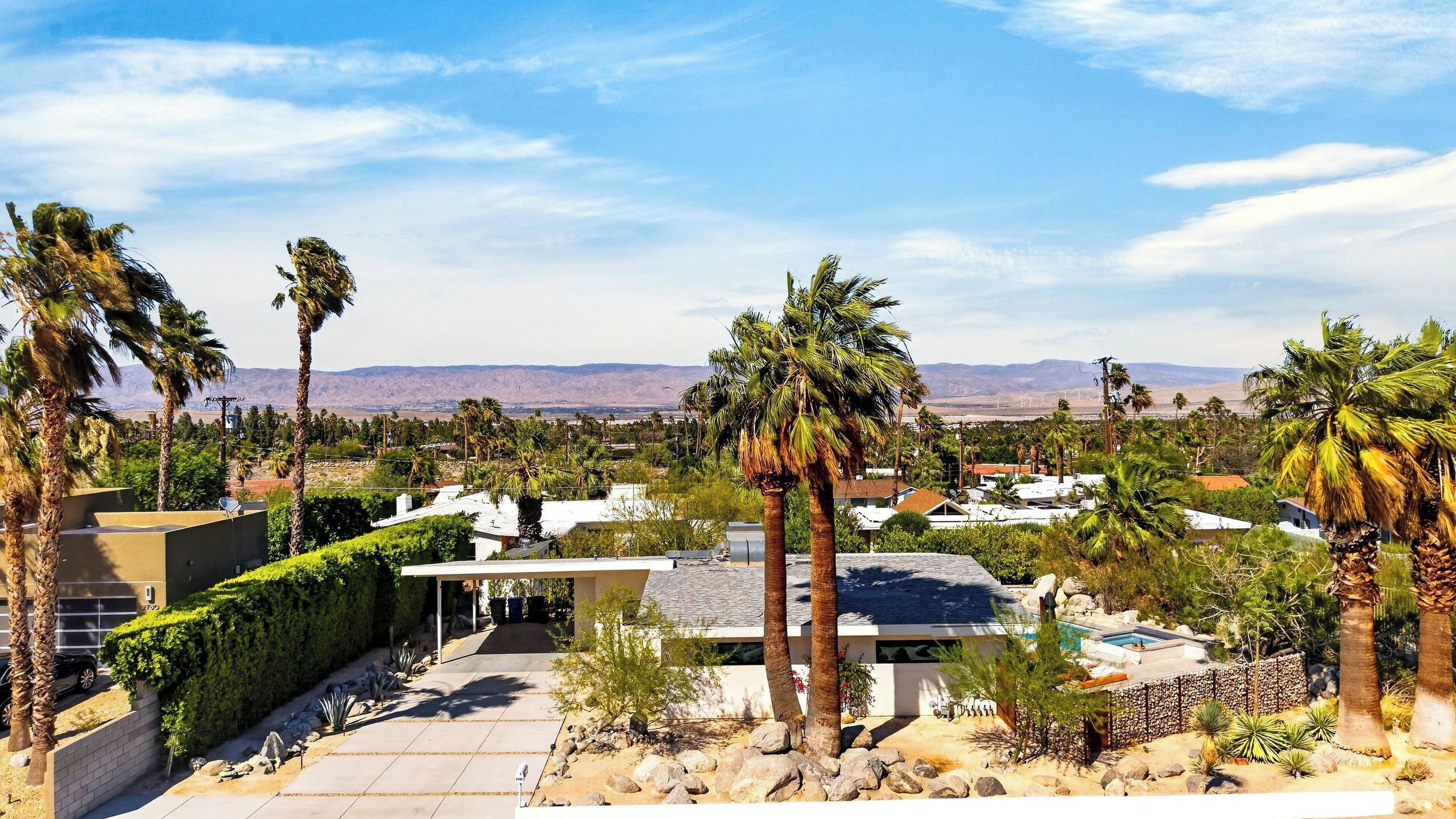 A residential area with modern houses, palm trees, and a clear view of distant mountains.
