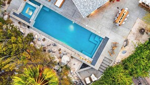 Ein rechteckiger Swimmingpool mit Whirlpool, umgeben von einer Terrasse mit Gartenmöbeln und Blick auf den Himmel.