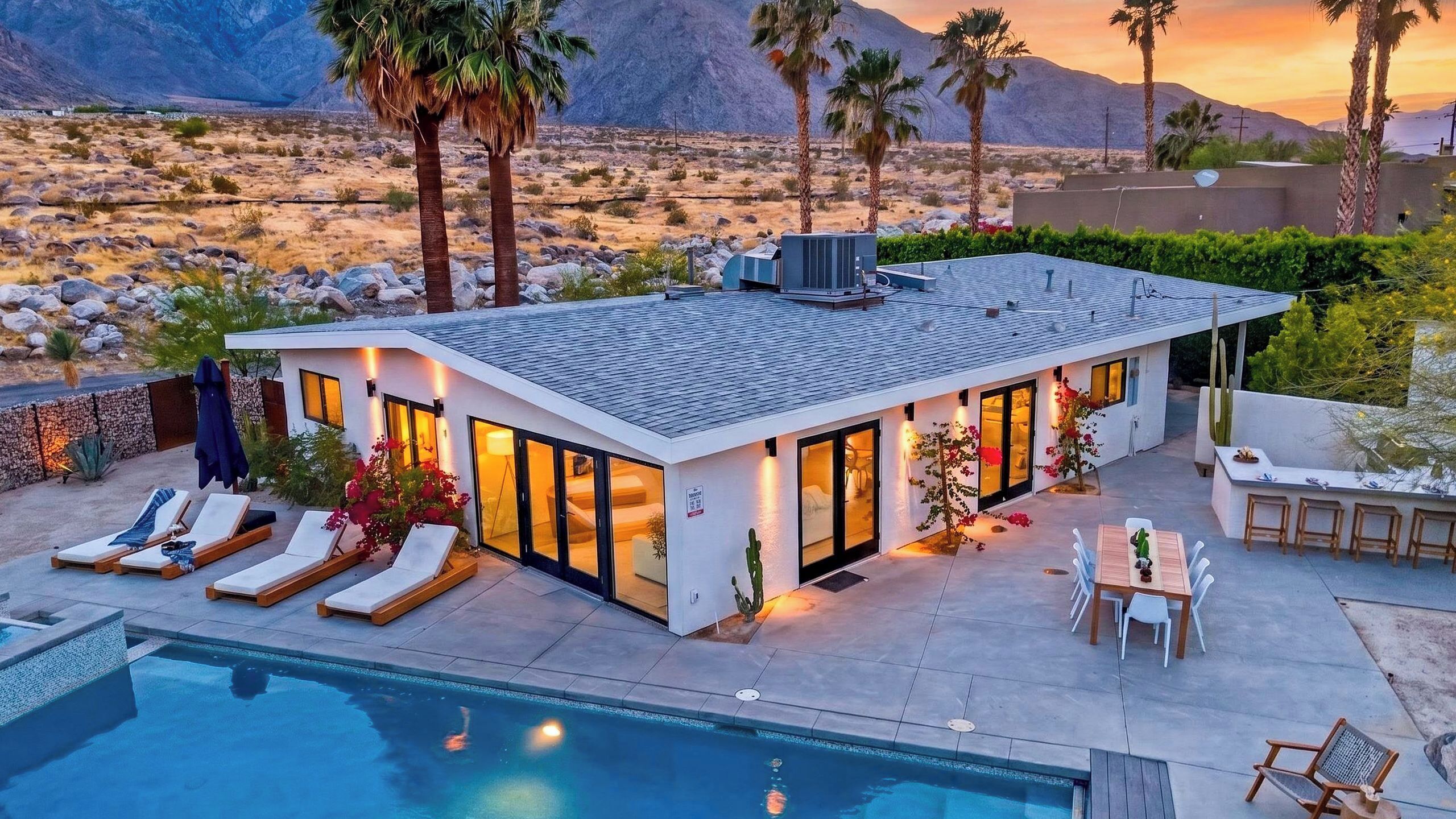 A modern house with a pool, lounge chairs, and a view of the desert landscape.