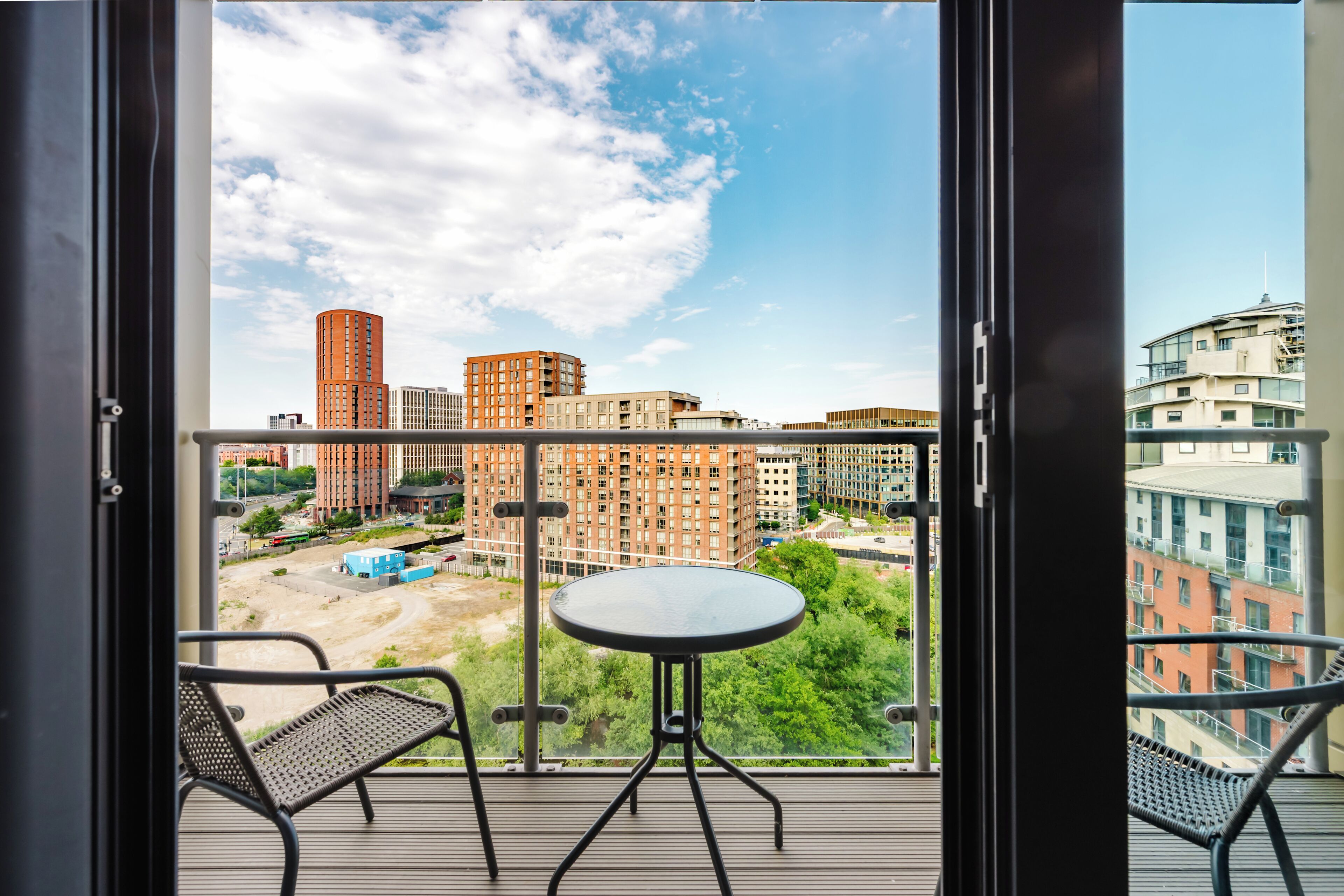 A balcony with a table and chairs, overlooking a cityscape with modern buildings.