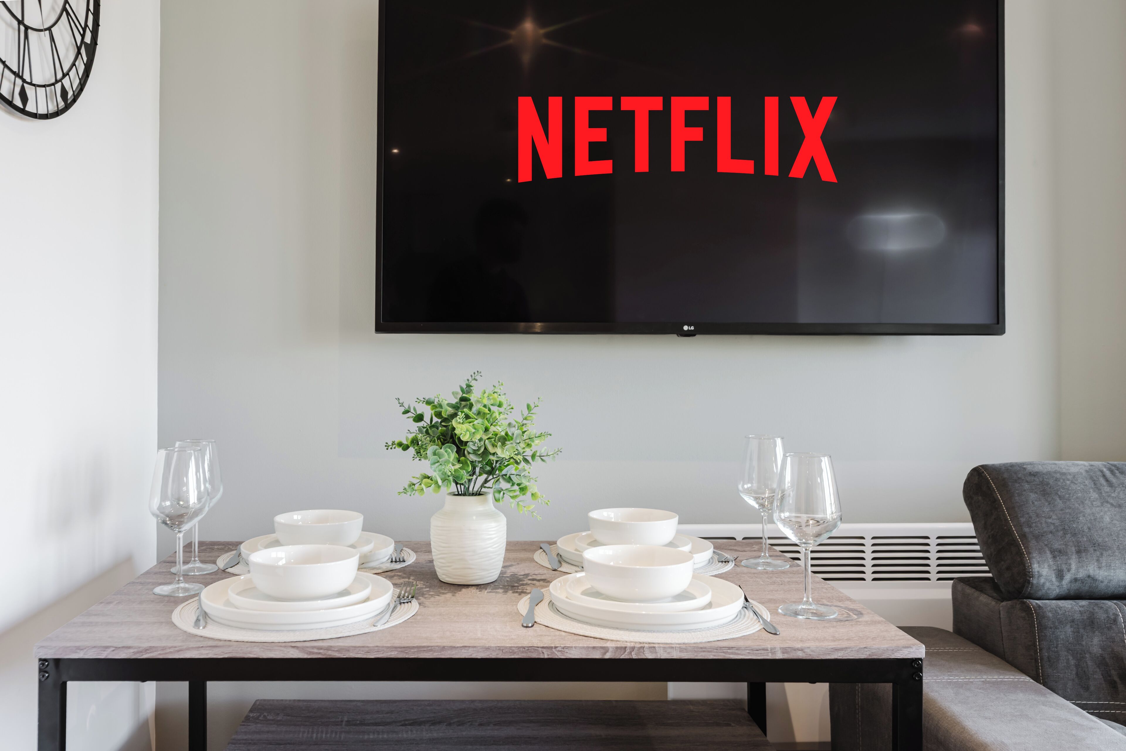 A dining area with a table set for four, a potted plant, and a TV screen displaying 'NETFLIX' in red letters.