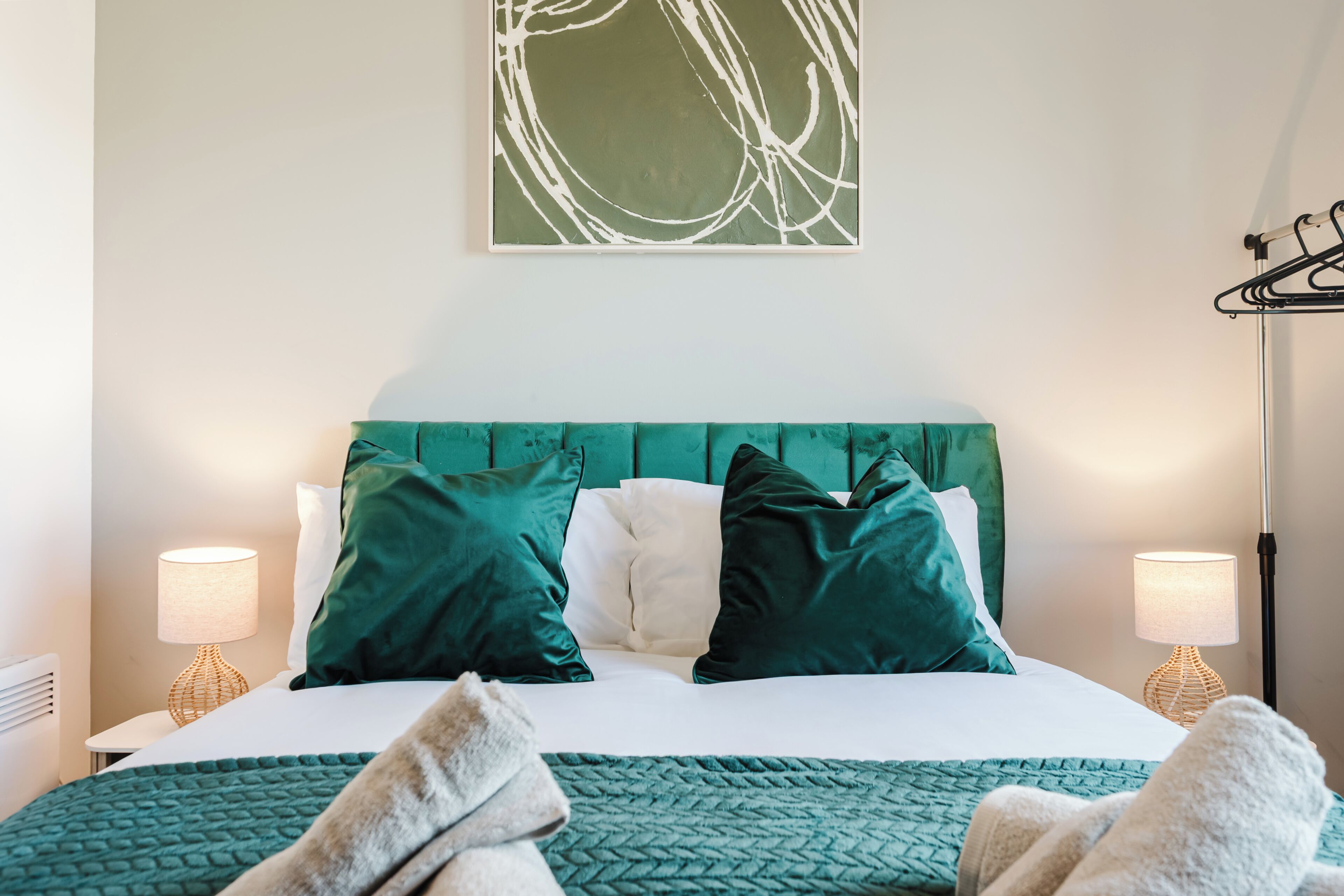A neatly made bed with a teal headboard, two pillows, and a green throw blanket.