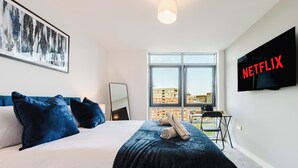 Et hotelværelse med seng, skrivebord, stol, fjernsyn og et vindue med udsigt over byen.