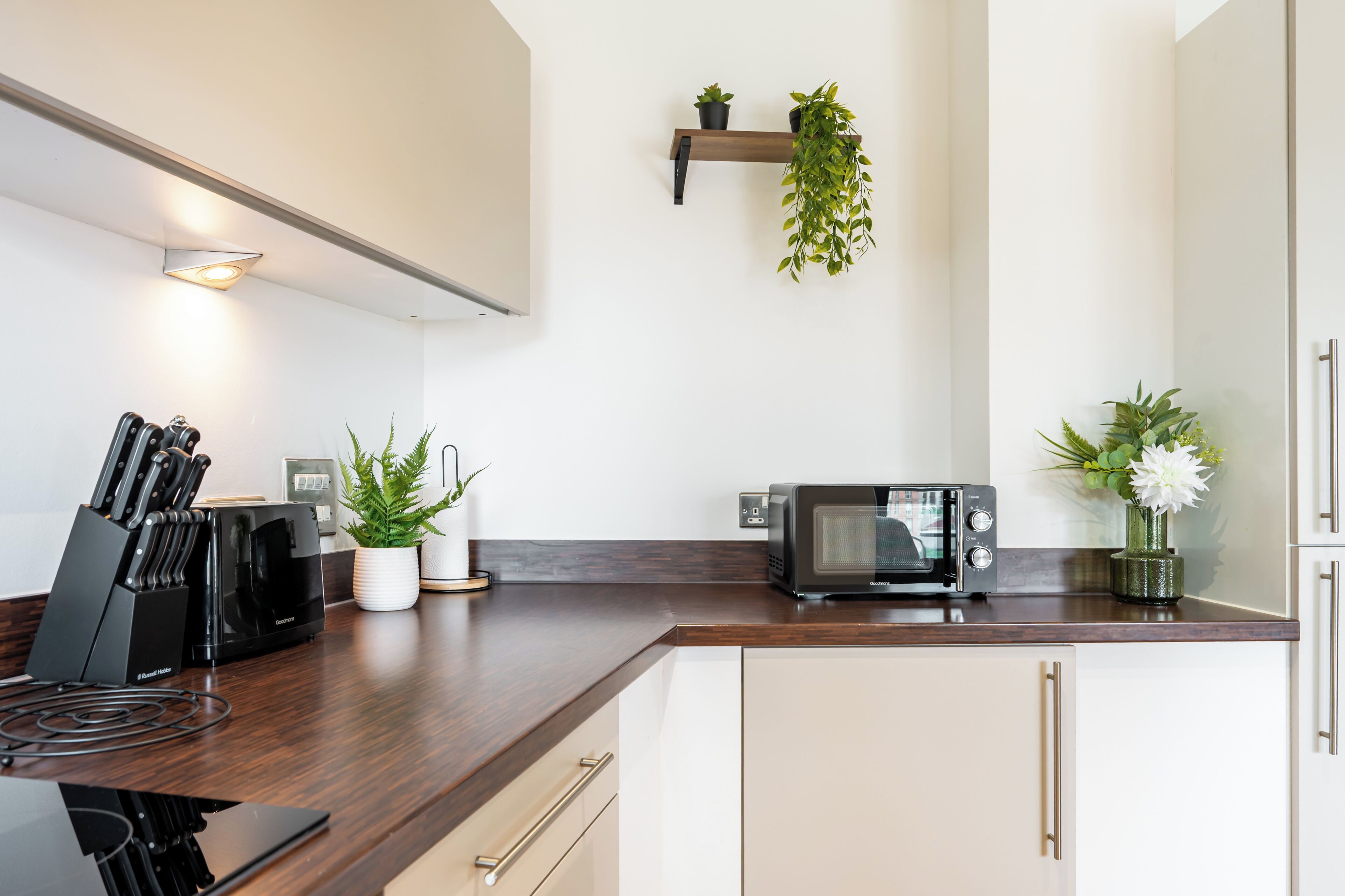 A modern kitchen with a built-in microwave, a knife block, and two potted plants.