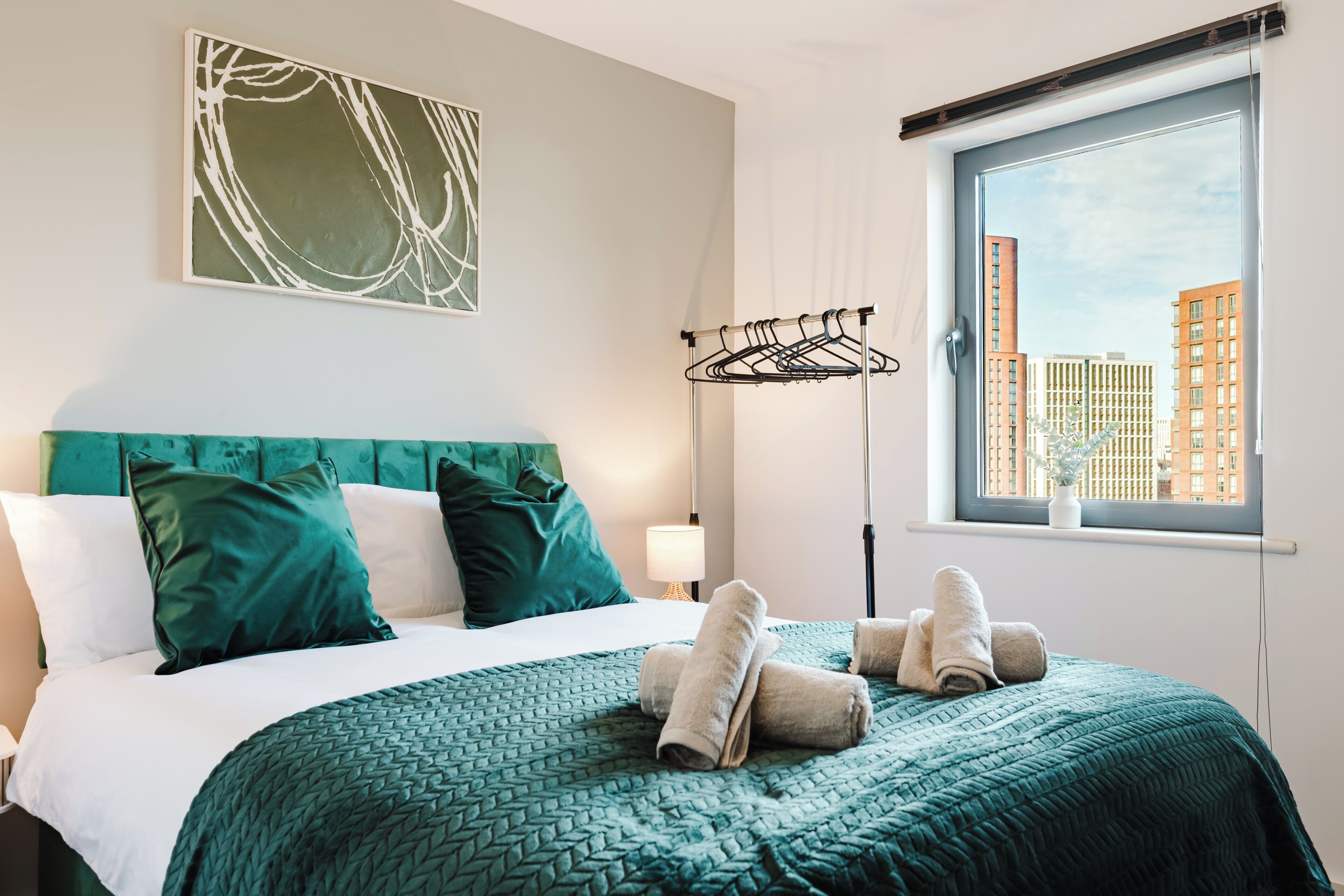 A hotel room with a bed, a window with a city view, and a wall-mounted drying rack.
