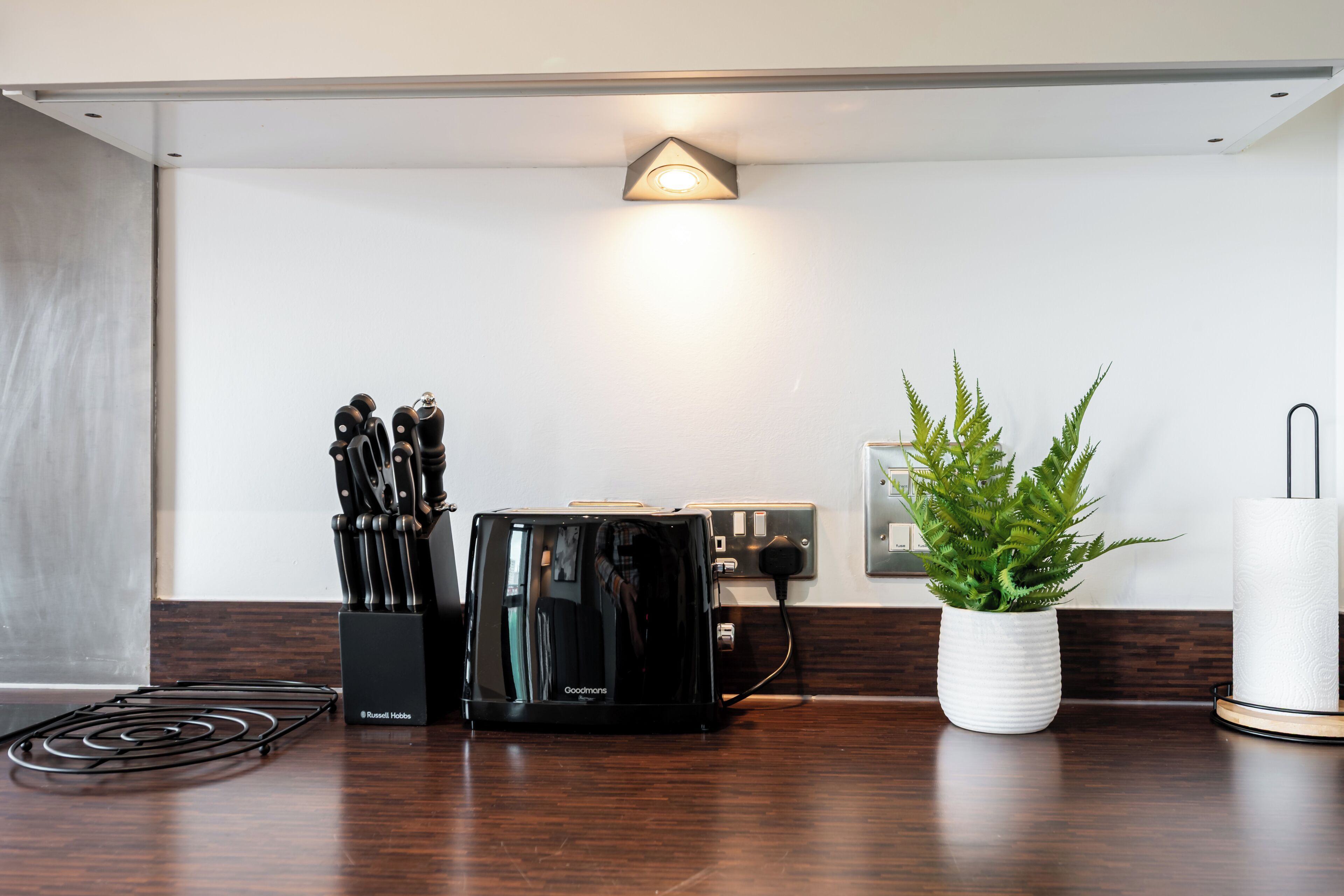 A kitchenette with a coffee maker, a knife block, and a potted plant.
