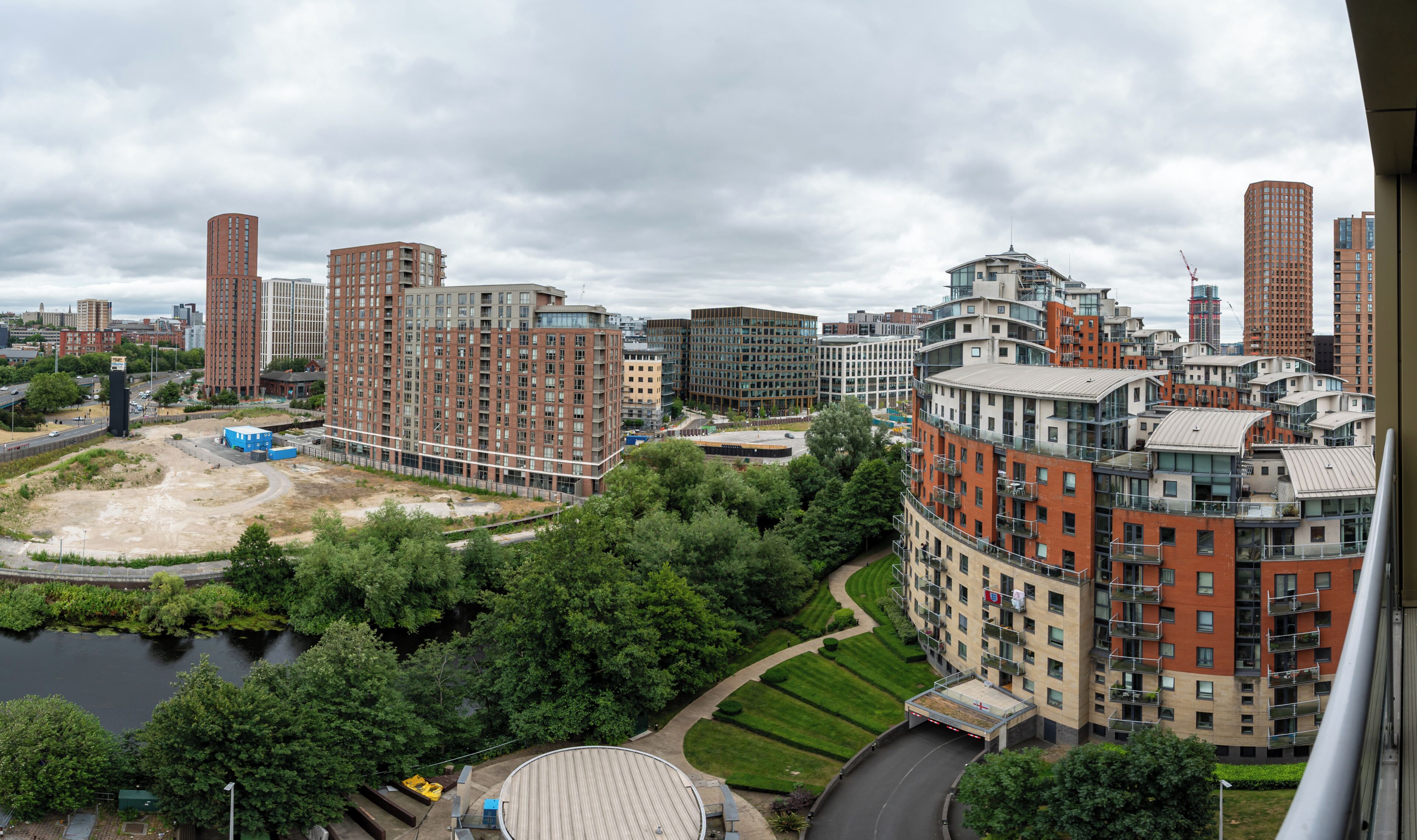 A high-rise residential building with multiple balconies, a river, and surrounding greenery.